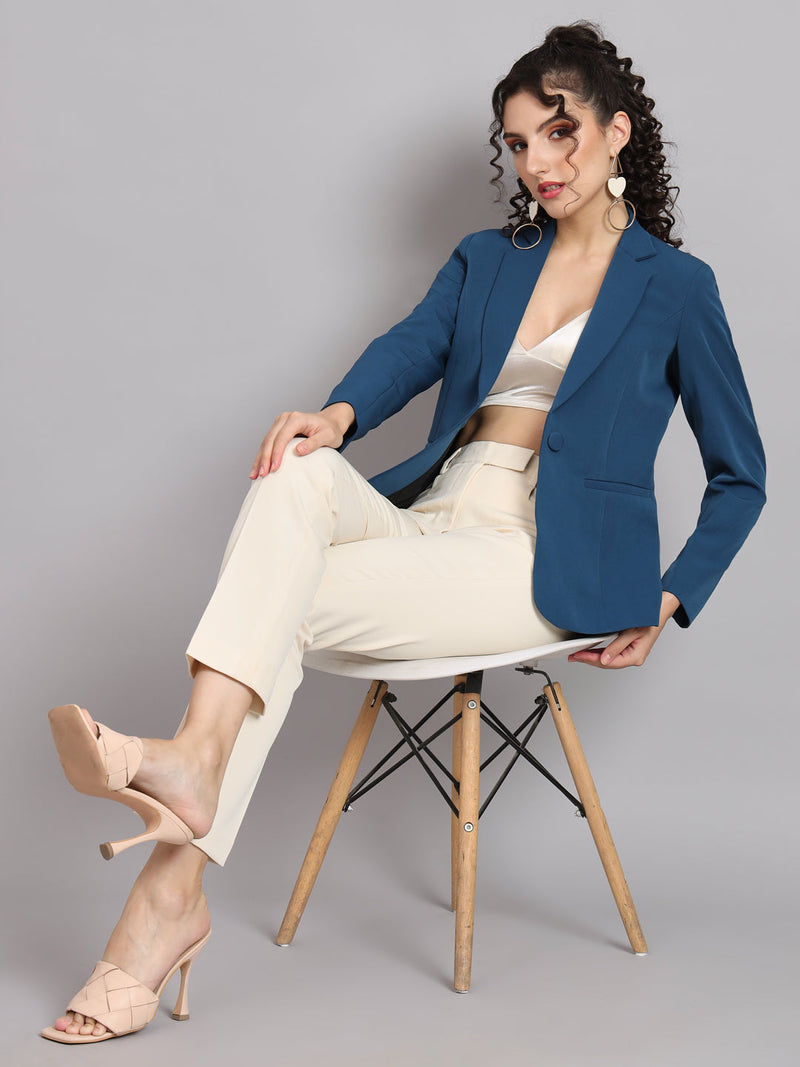 Notched collar teal blue polyester blazer styled with cream trousers and heels.